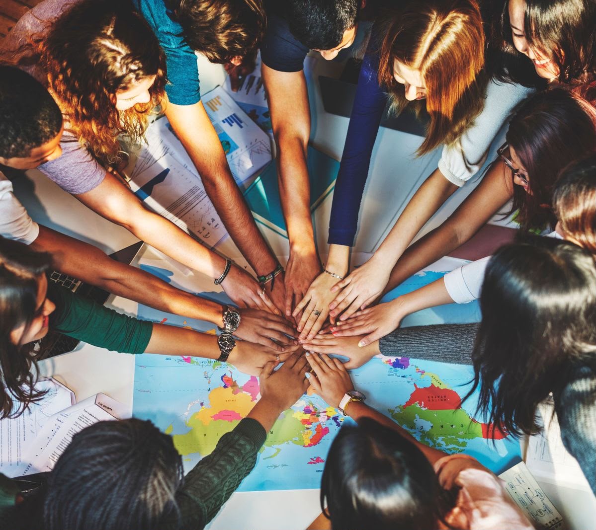 Young people joining hands in a circle over a world map